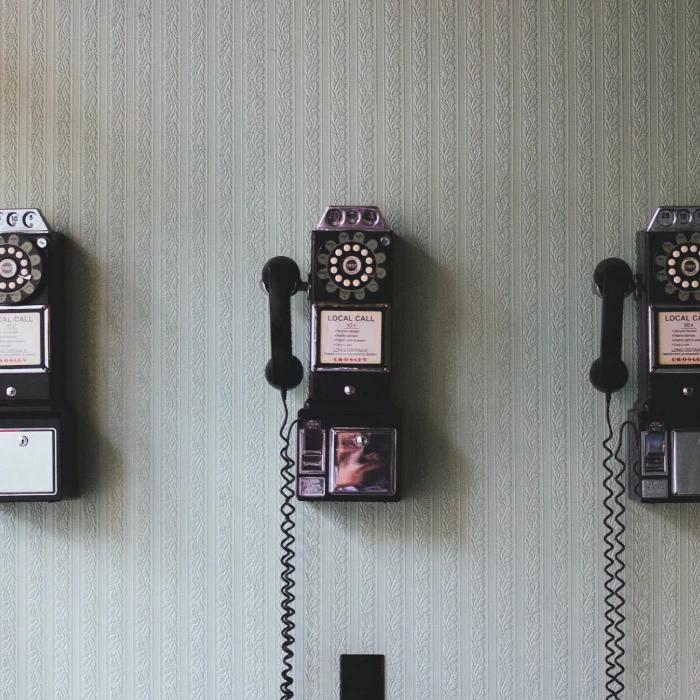 Tres tel&eacute;fonos de disco vintage colgados en una pared con papel tapiz verde.