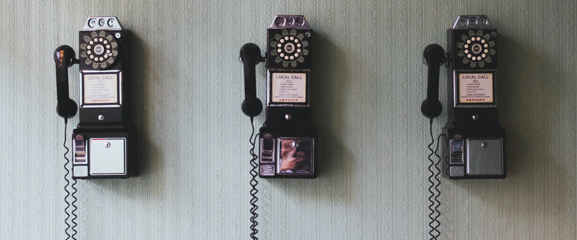 Tel&eacute;fonos antiguos de pago en una pared con fondo de papel tapiz verde.