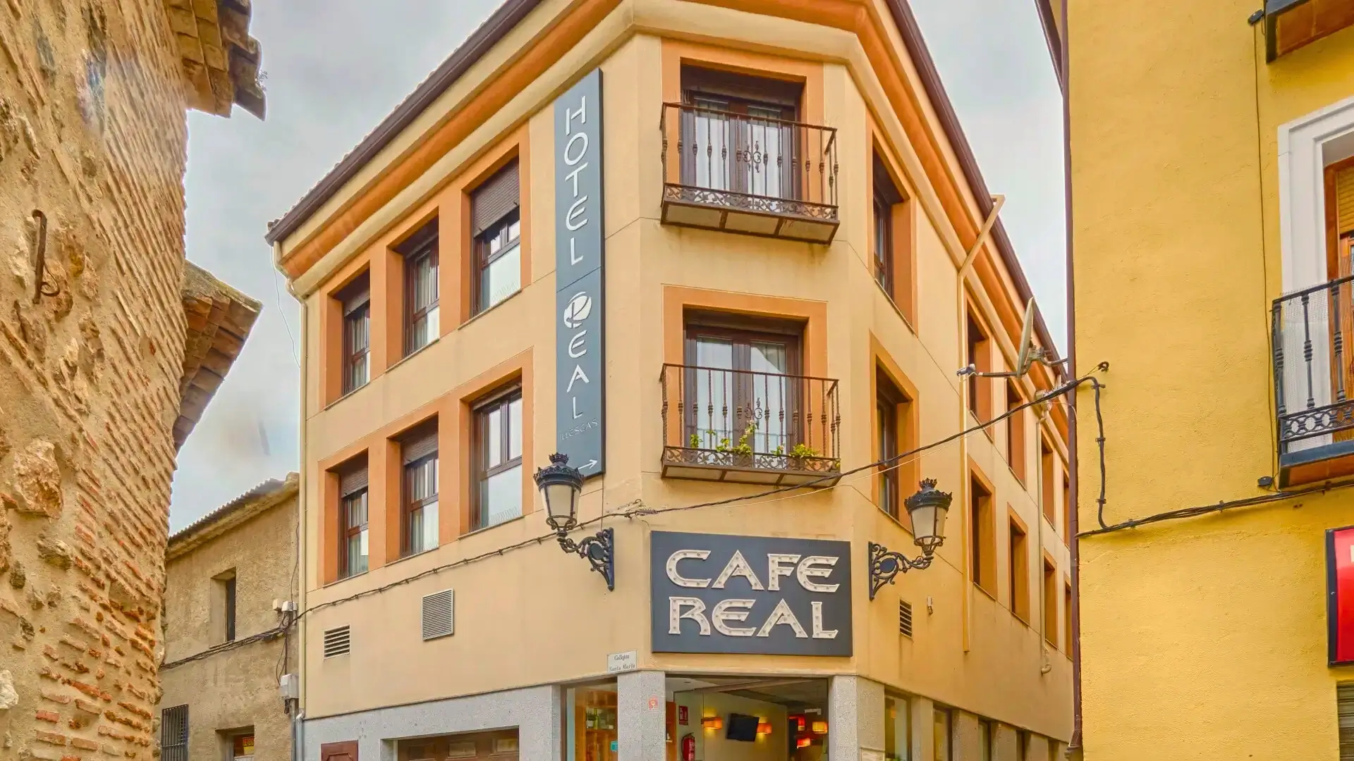 Edificio de esquina con letrero de Hotel y Caf&eacute; Real, balcones y faroles.