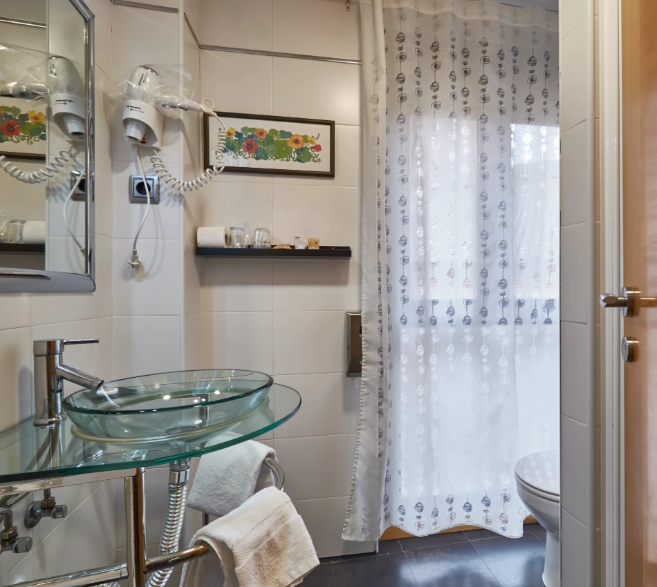 Ba&ntilde;o con tapa de vidrio en el lavabo y cortinas blancas decoradas con patrones.