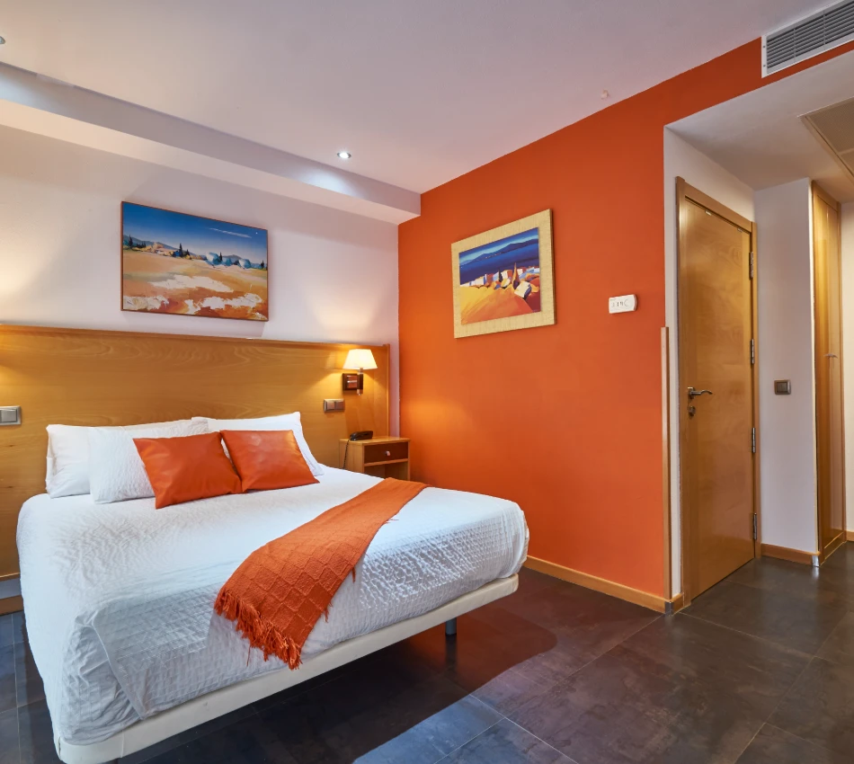 Habitaci&oacute;n con cama doble, paredes naranjas y decoraciones de playa.