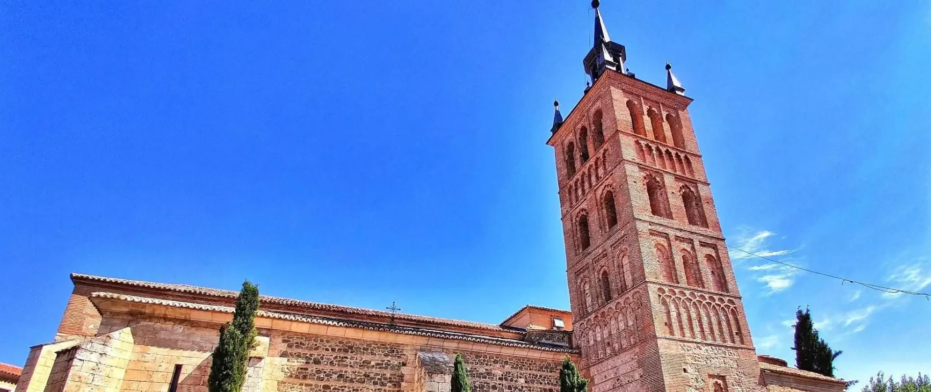 Torre de ladrillo sobre edificio hist&oacute;rico bajo un cielo azul claro.