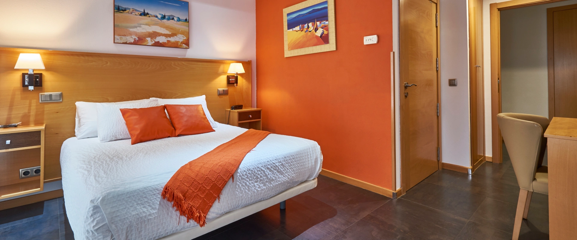 Habitaci&oacute;n de hotel con cama, decoraciones y paredes en tonos naranjas.
