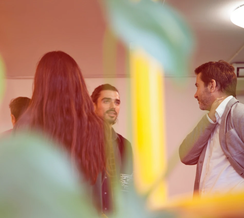 Personas conversando en interior con plantas borrosas en primer plano.