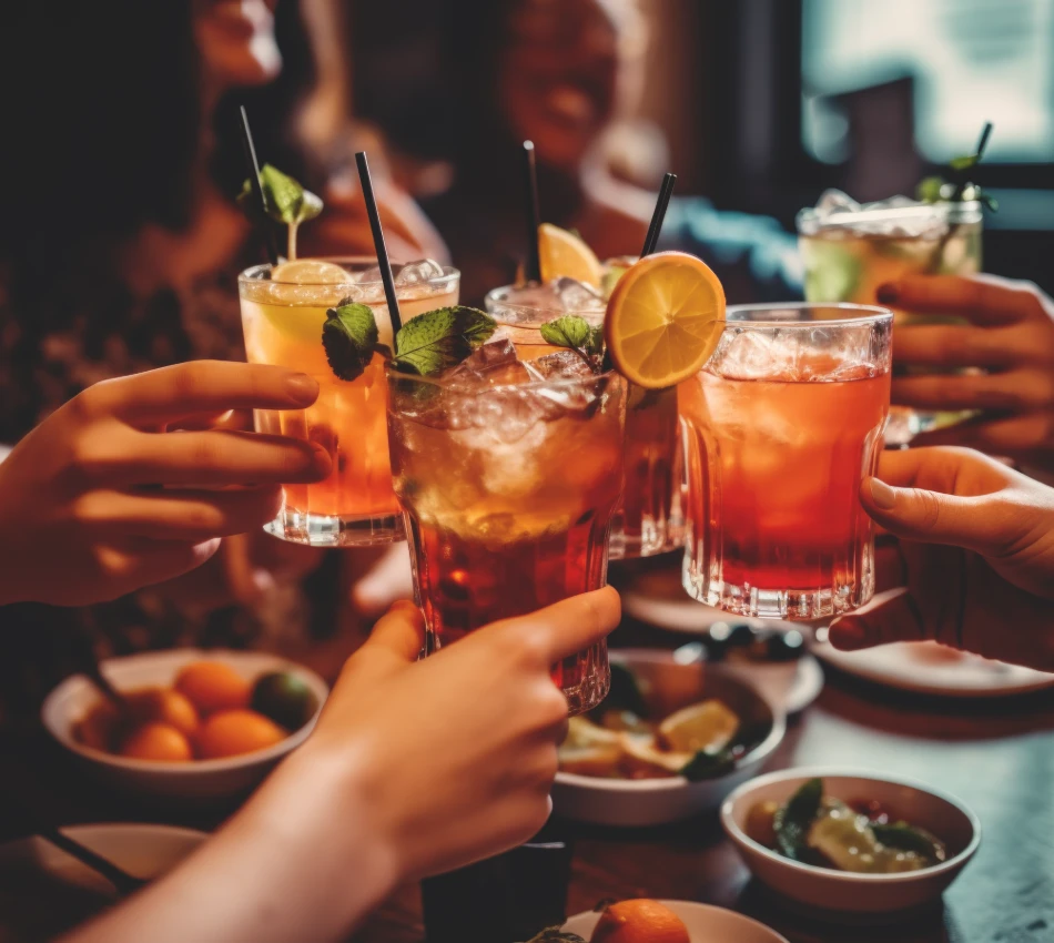 Personas brindando con c&oacute;cteles y rodajas de lim&oacute;n sobre una mesa con comida.