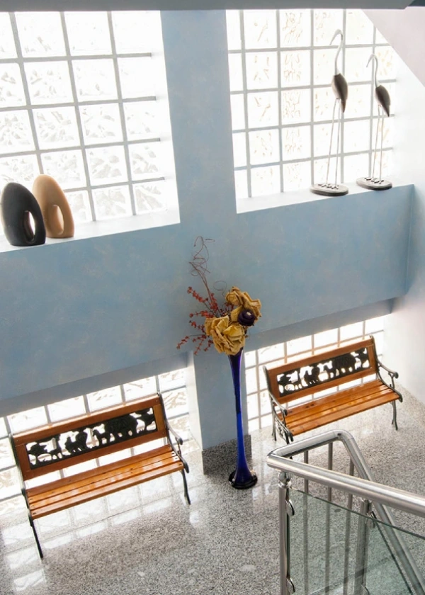 Escalera moderna con bancos, jarr&oacute;n azul y figuras en la pared con vidrio bloc.