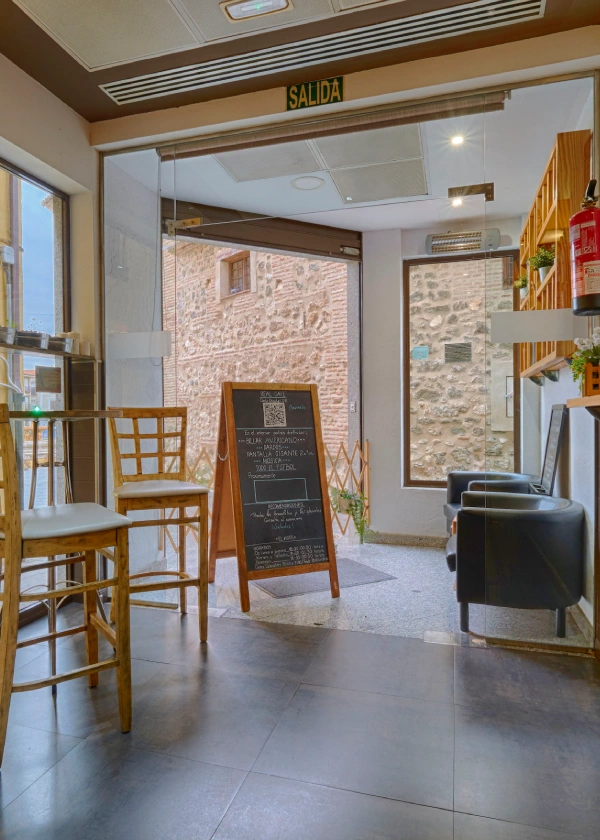 Interior de una cafeter&iacute;a con puerta de vidrio y pizarra junto a la salida.