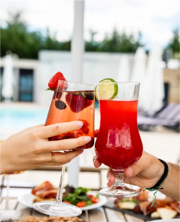 Duas pessoas brindando com drinks coloridos ao ar livre.