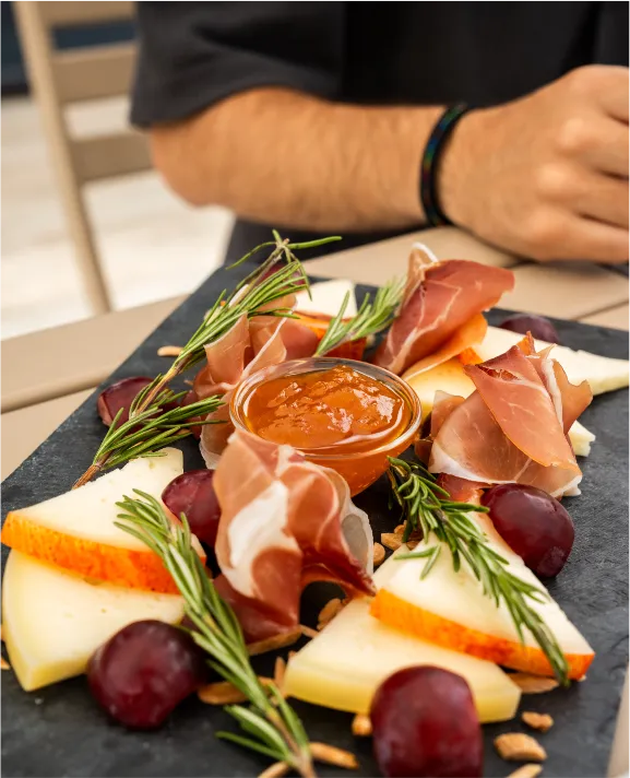 Prato com queijos, presunto, uvas e molho, decorado com alecrim.