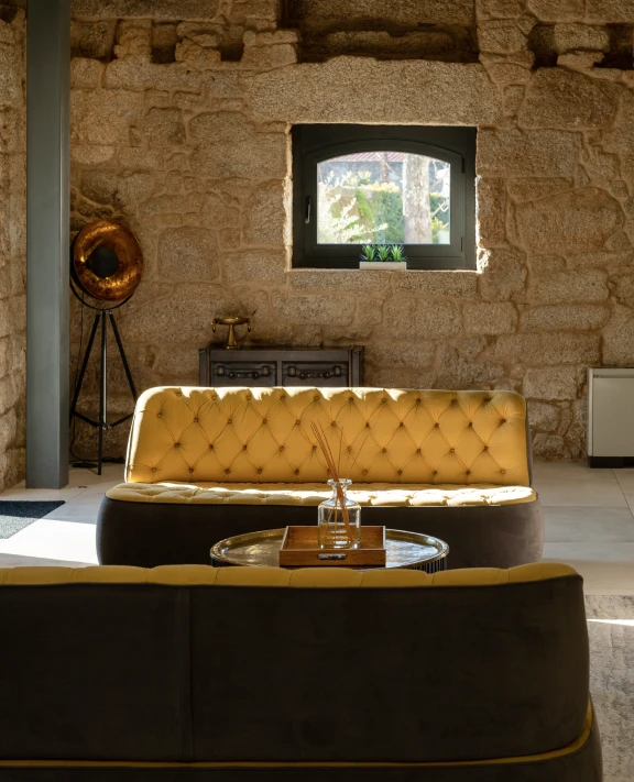 Sala com sofás amarelos, janela de pedra e decoração rústica.