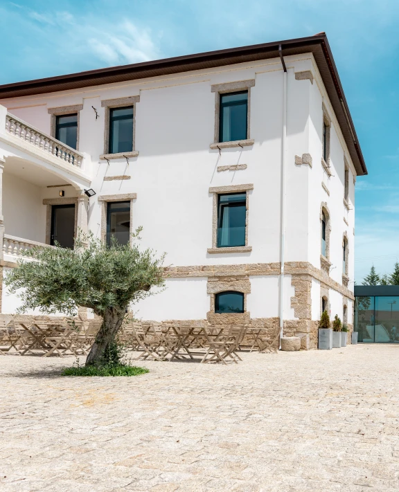 Edifício branco com áreas de pedra e árvore na frente.