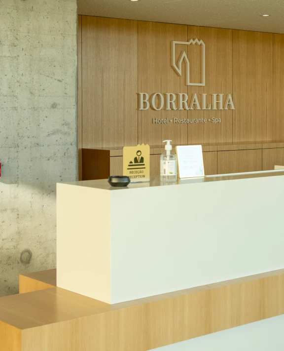 Recepção de hotel com placa "BORRALHA" e itens sobre o balcão.
