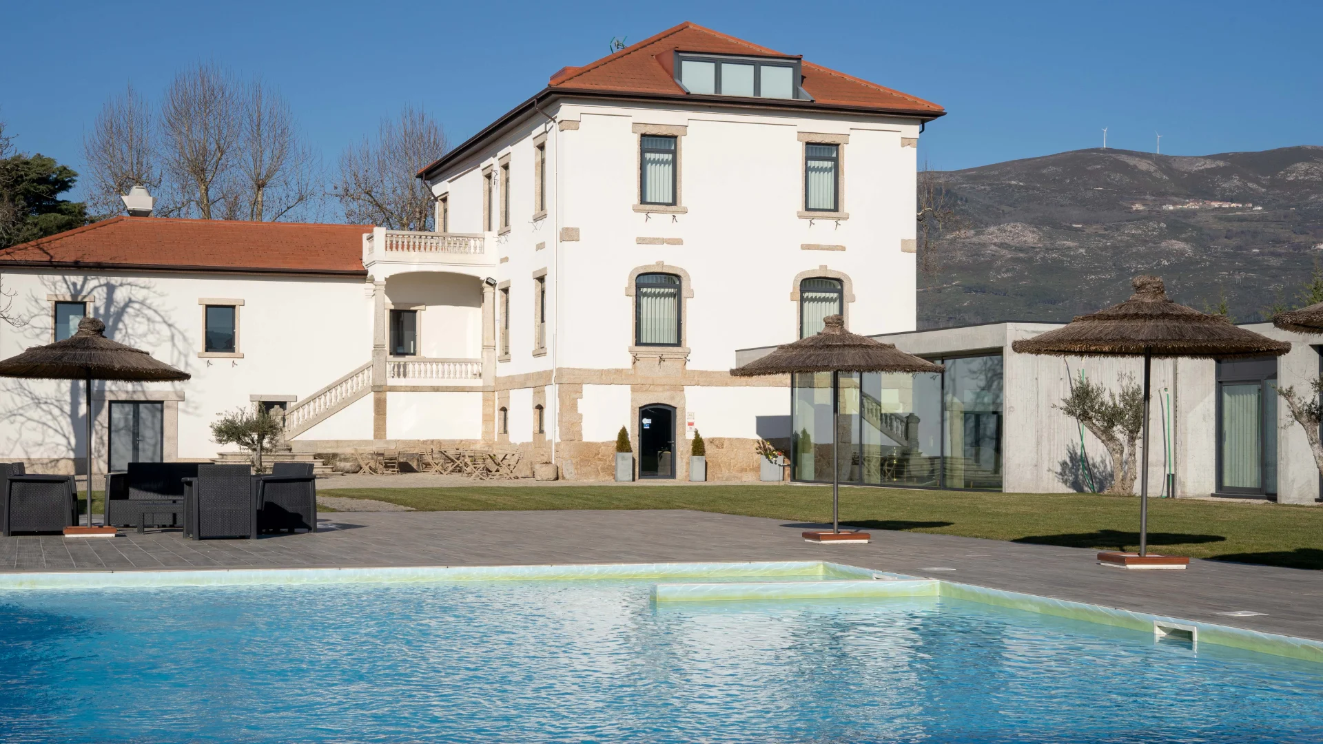 Mans&atilde;o com piscina, guarda-s&oacute;is e montanha ao fundo em dia ensolarado.