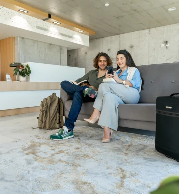 Casal sorrindo sentado em sagu&atilde;o com bagagens ao lado.