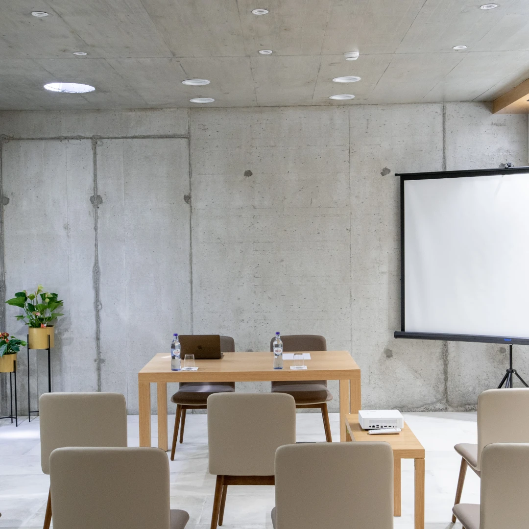 Sala de confer&ecirc;ncias vazia com cadeiras e mesa. Tela de proje&ccedil;&atilde;o &agrave; direita.