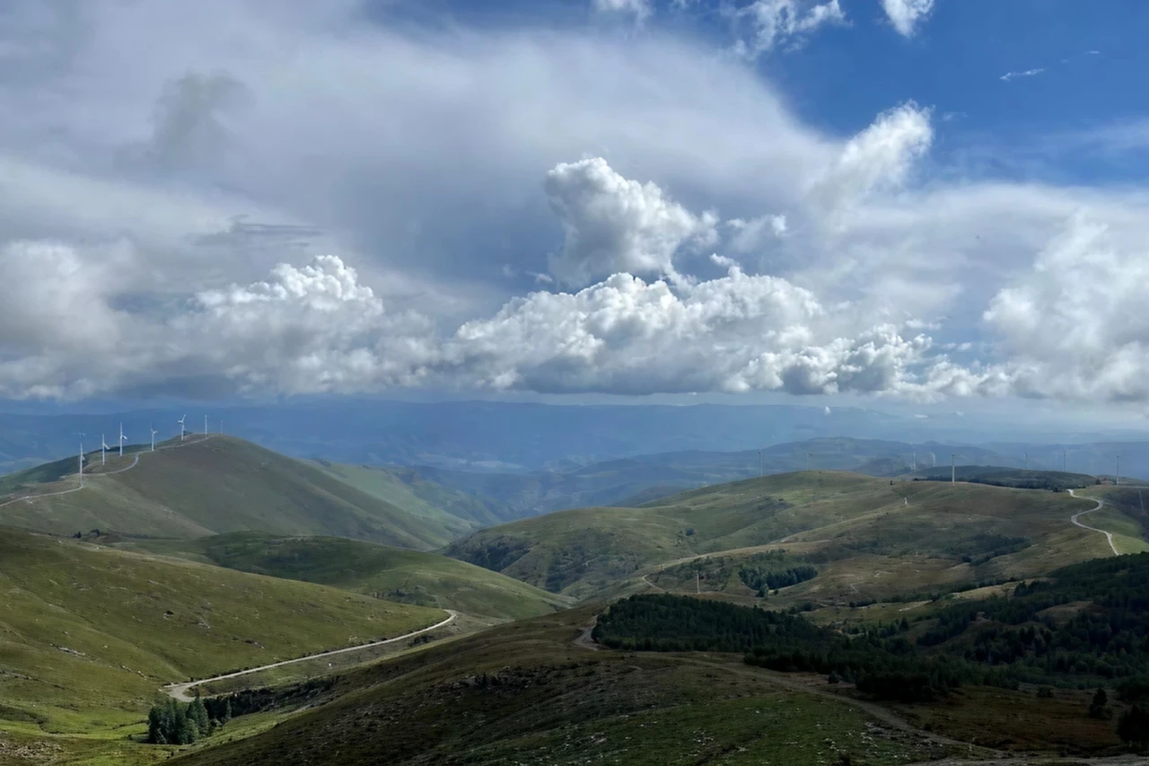 Paisagem montanhosa com turbinas e&oacute;licas e c&eacute;u nublado.