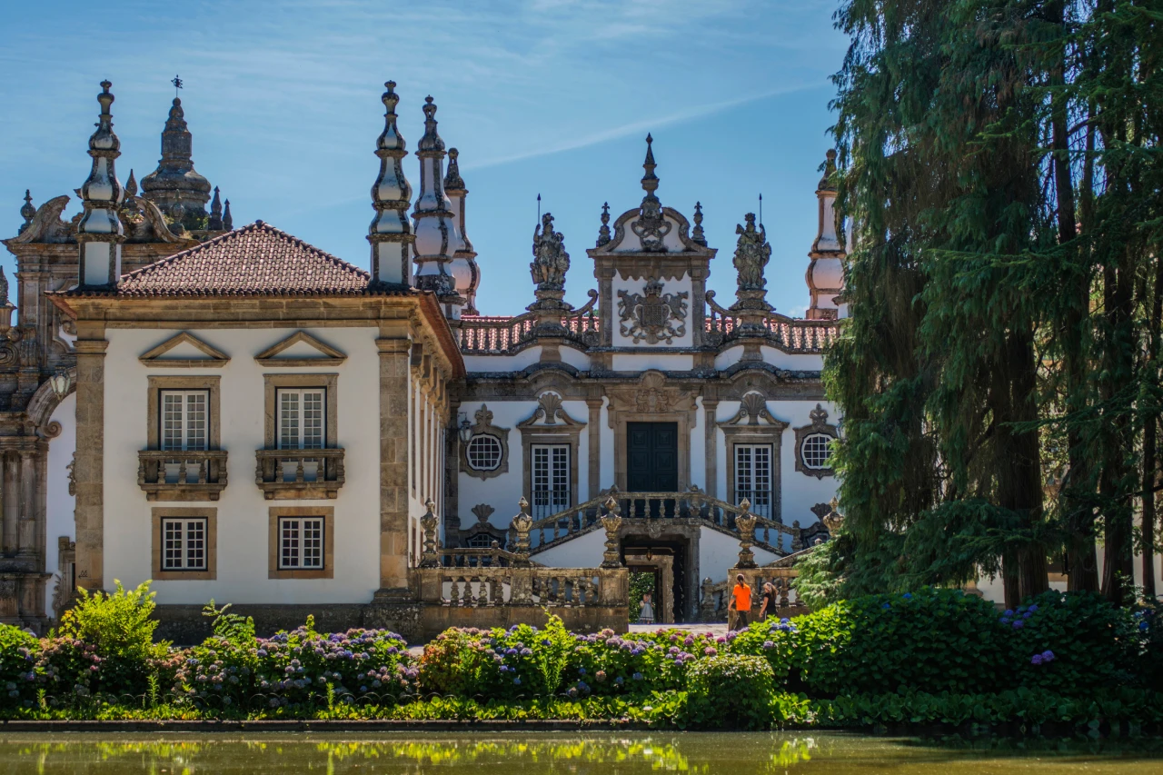 Pal&aacute;cio com jardins floridos e c&eacute;u azul ao fundo.