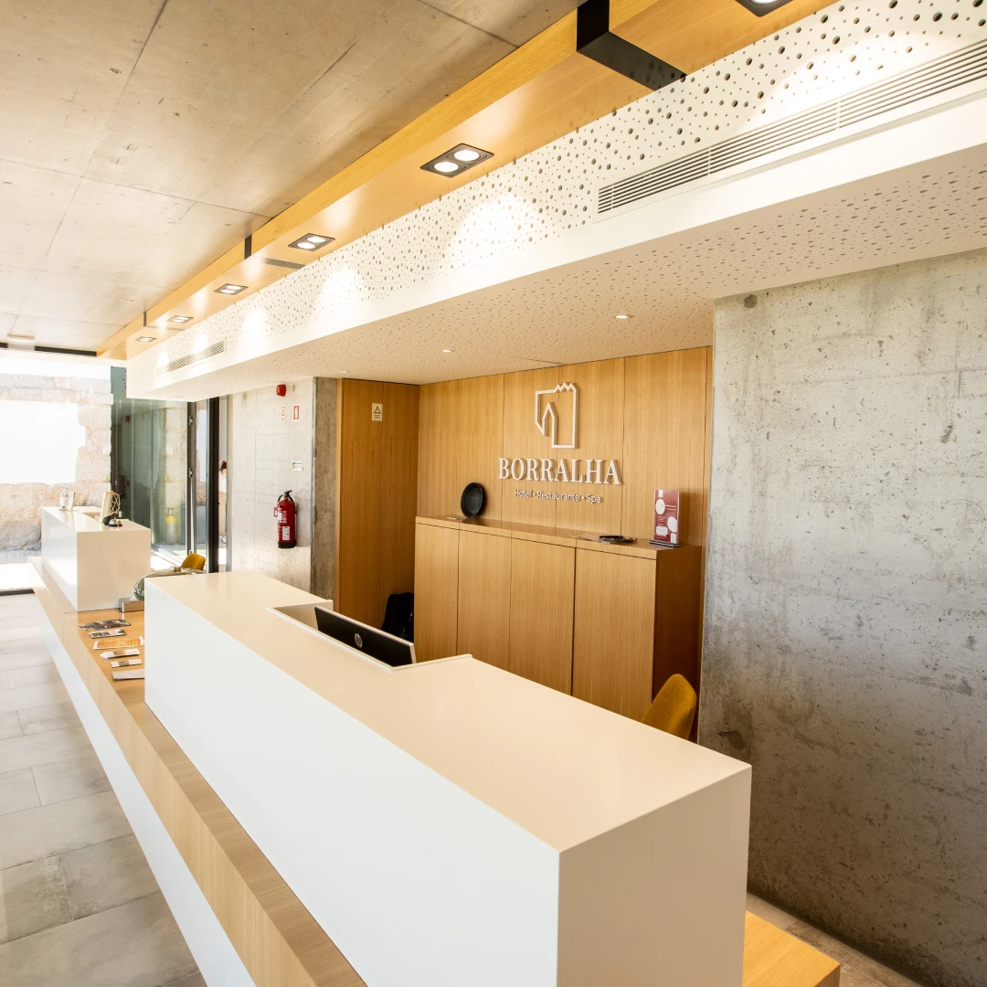 Recep&ccedil;&atilde;o moderna de um hotel com balc&atilde;o branco e parede de madeira.