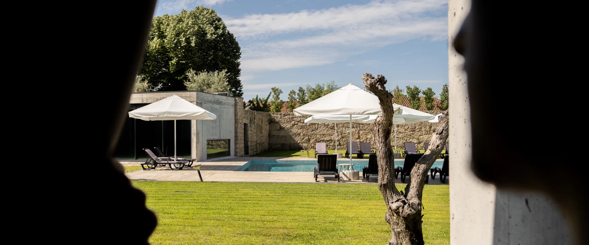Piscina ao ar livre com guarda-s&oacute;is em &aacute;rea verde e c&eacute;u azul.