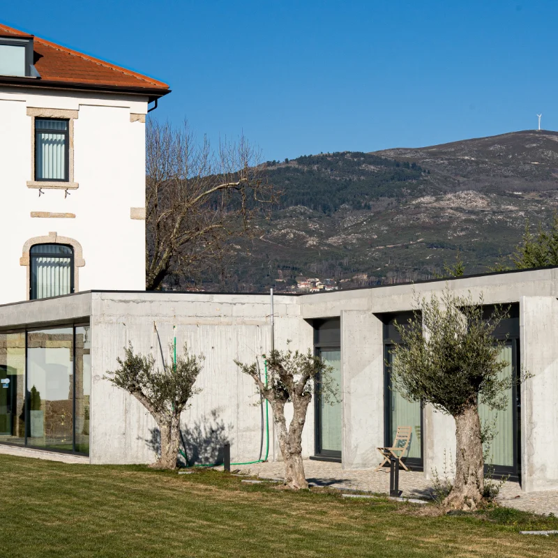 Casar&atilde;o branco junto a anexo moderno e montanha ao fundo.