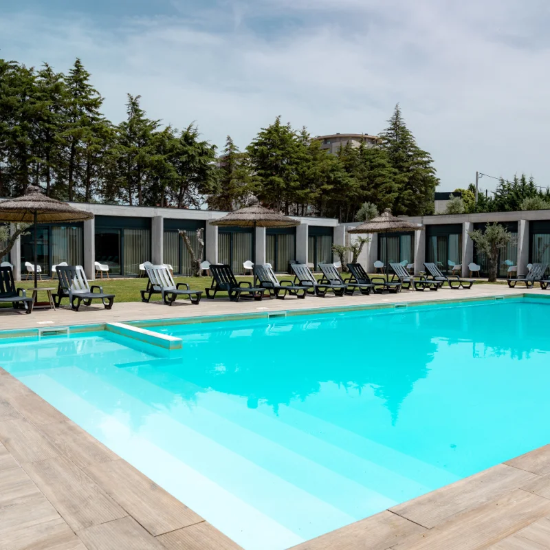 Piscina ao ar livre com espregui&ccedil;adeiras e cabanas ao fundo.