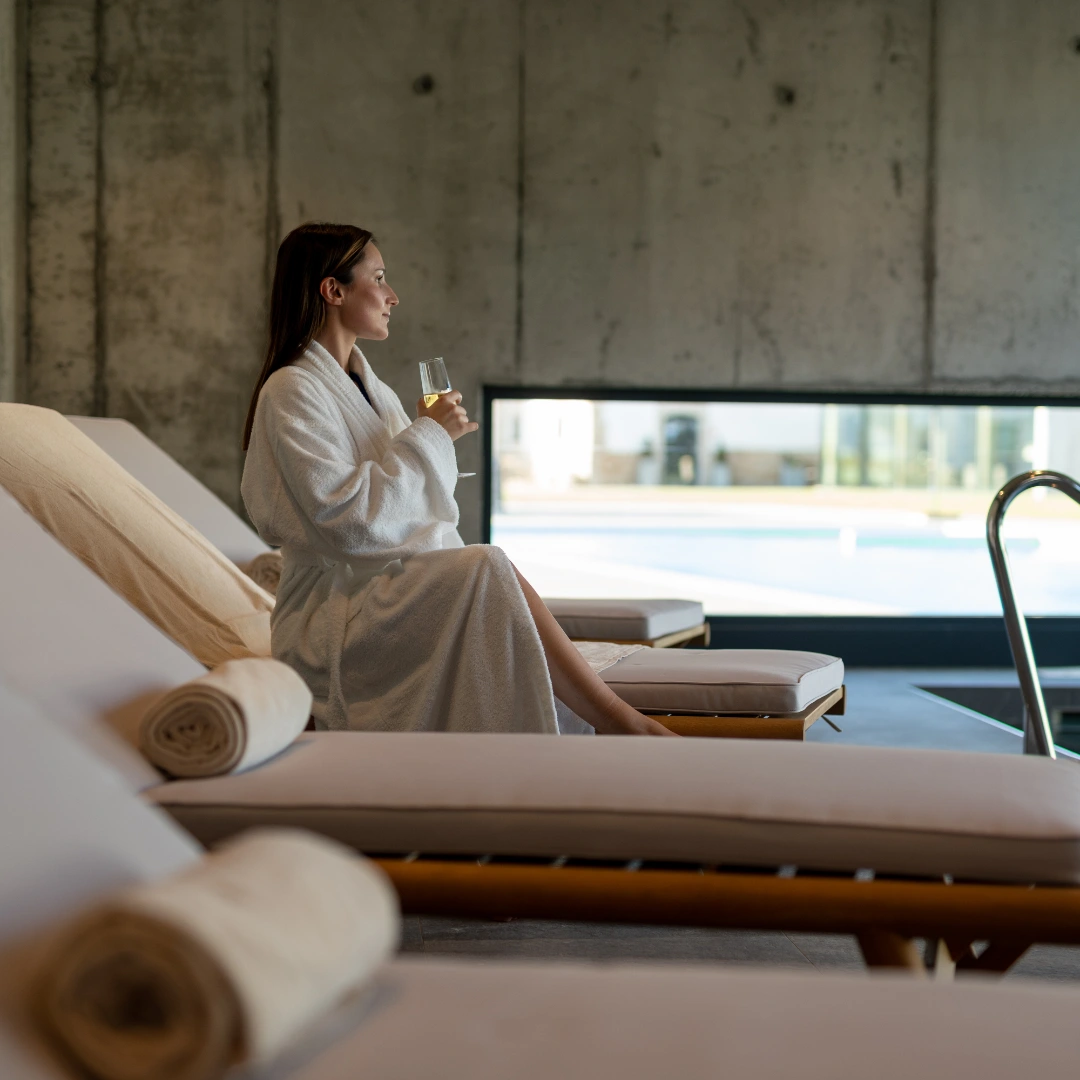 Mulher relaxando em espregui&ccedil;adeira com ta&ccedil;a de espumante em ambiente de spa.