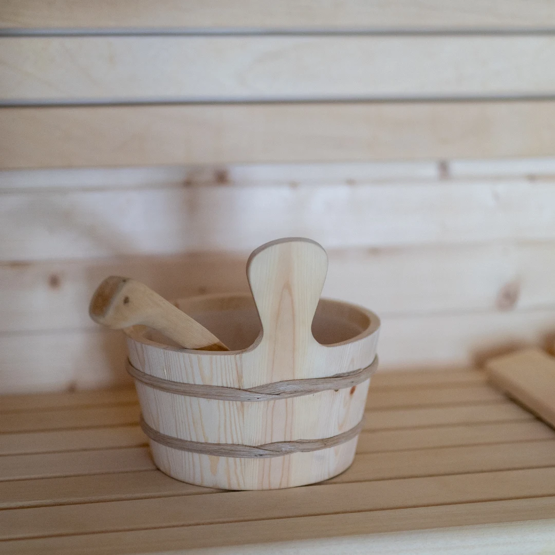 Balde de madeira e concha em sauna de madeira clara.