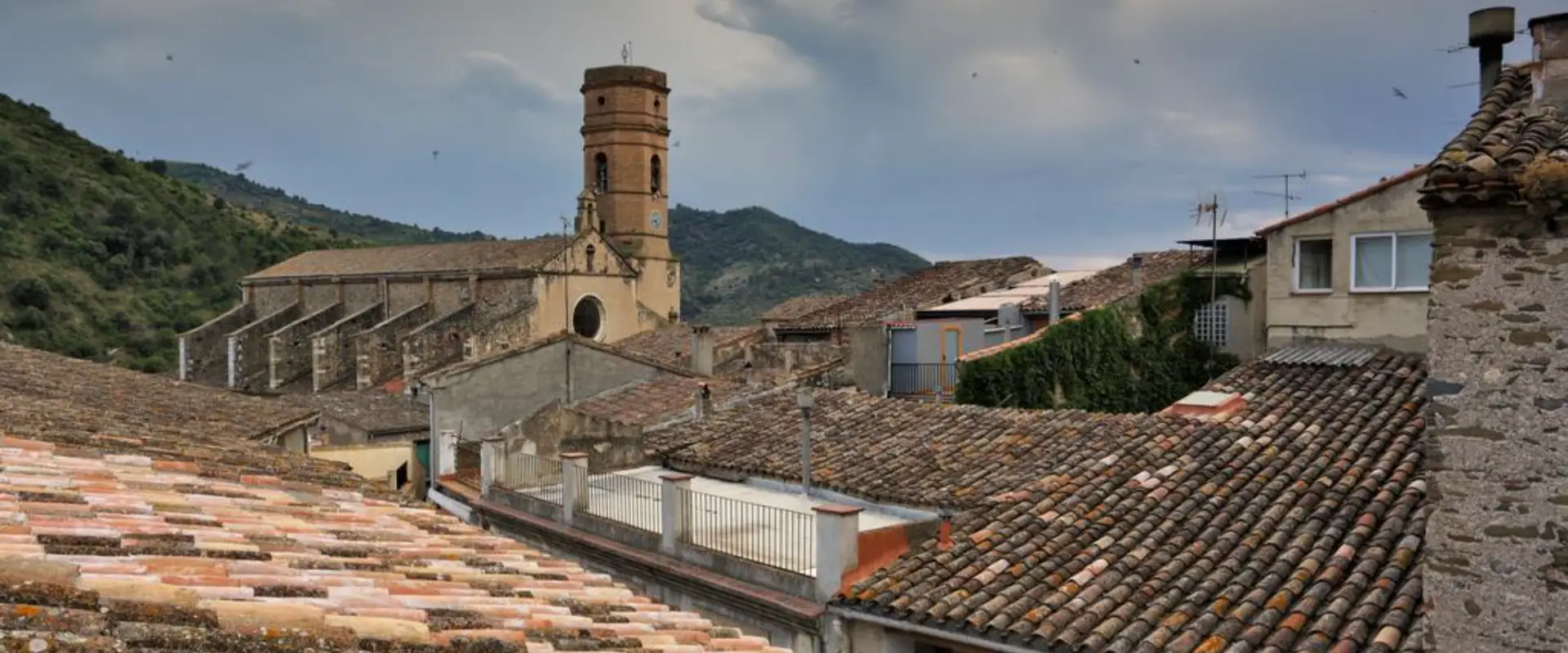 Vista de teulades amb torre i muntanyes al fons.