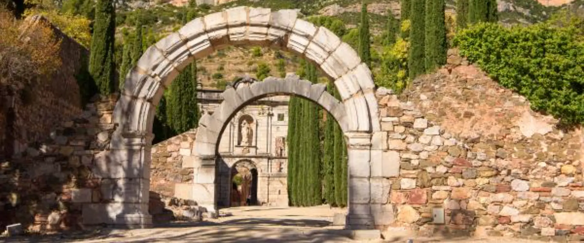Arc de pedra davant un edifici hist&ograve;ric amb xiprers al voltant.