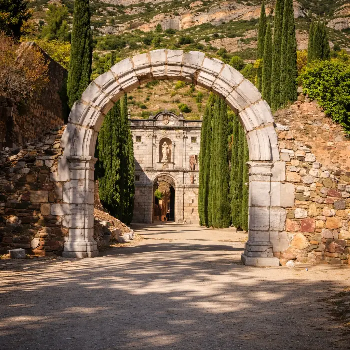 Arc de pedra amb ciprers i una fa&ccedil;ana antiga al fons.