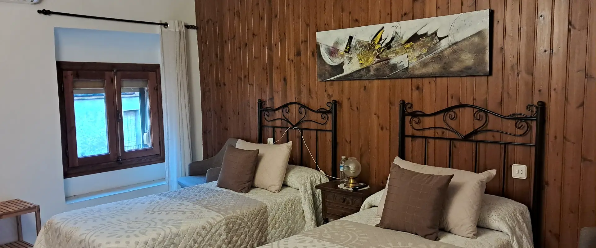 Habitaci&oacute; amb dues llits individuals, paret de fusta i quadre abstracte.