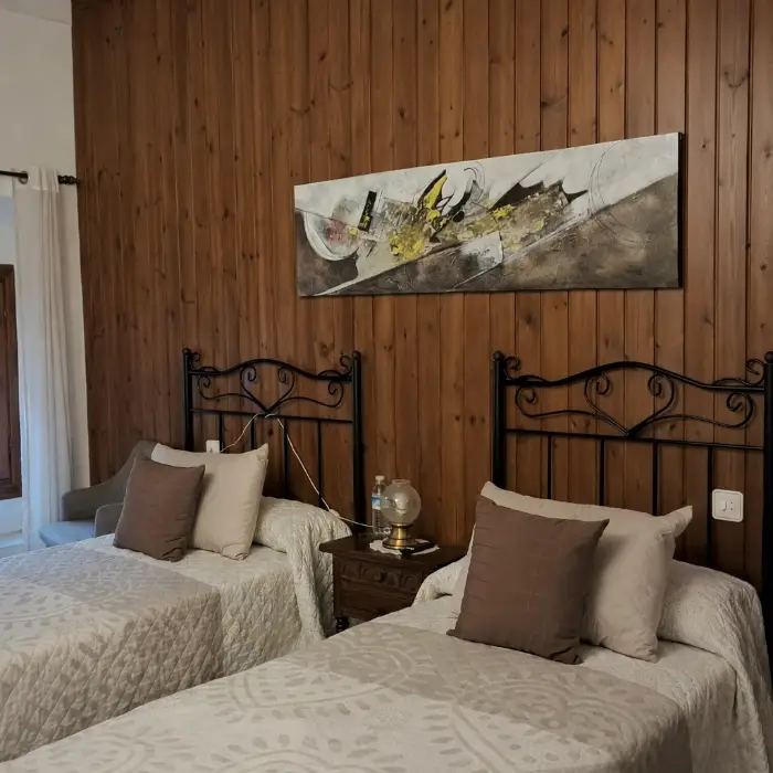 Habitaci&oacute; amb dues llits, paret de fusta i quadre abstracte.