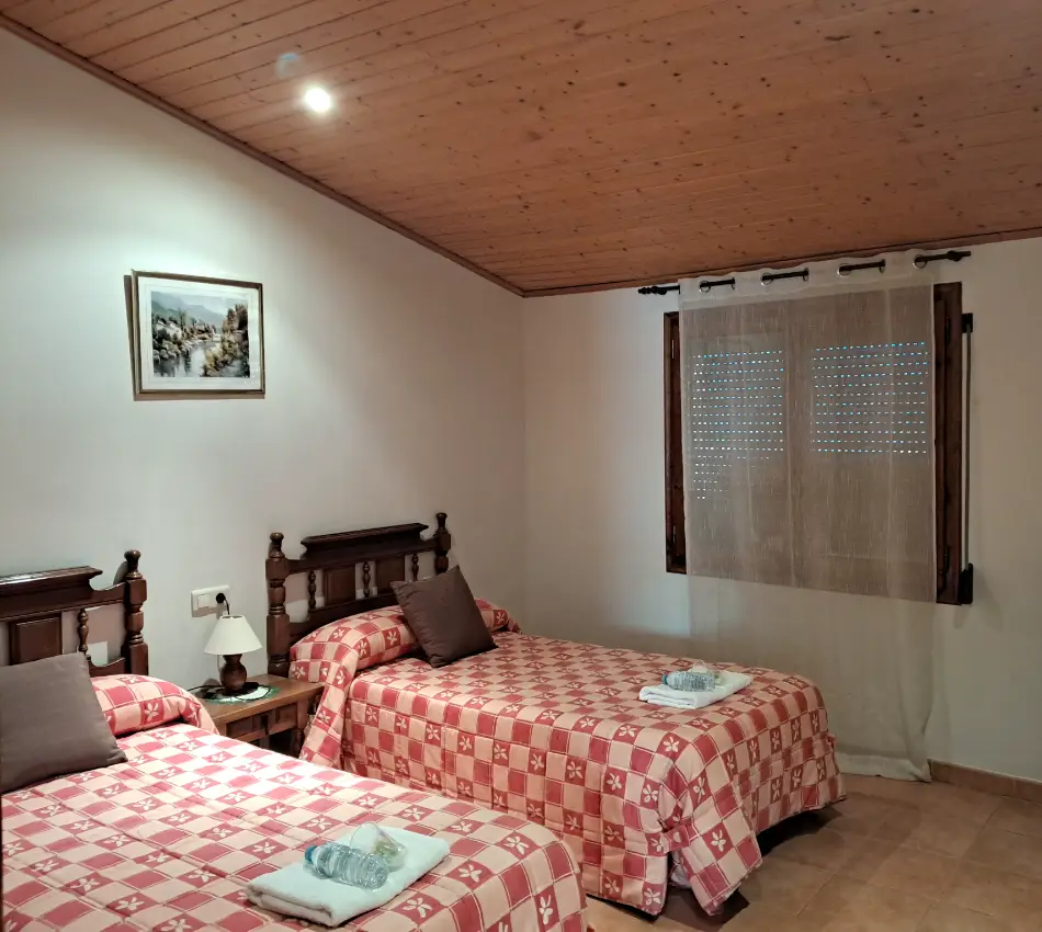 Habitaci&oacute; amb dues llits individuals amb cobrellits quadriculats vermells i blancs.