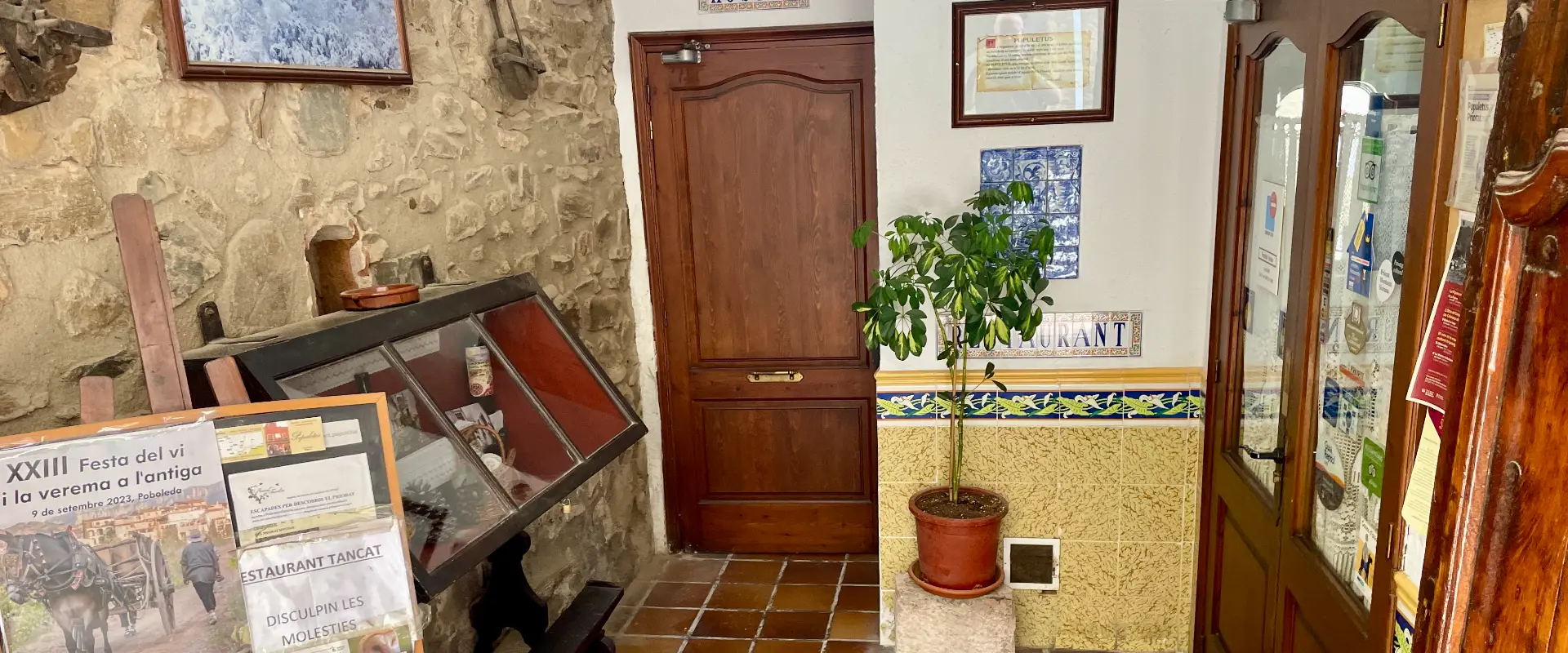 Antic rebost amb porta de fusta, planta i cartells sobre festa del vi.