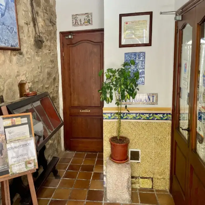Interior de restaurant, porta de fusta, cartell "TANCAT", planta decorativa.
