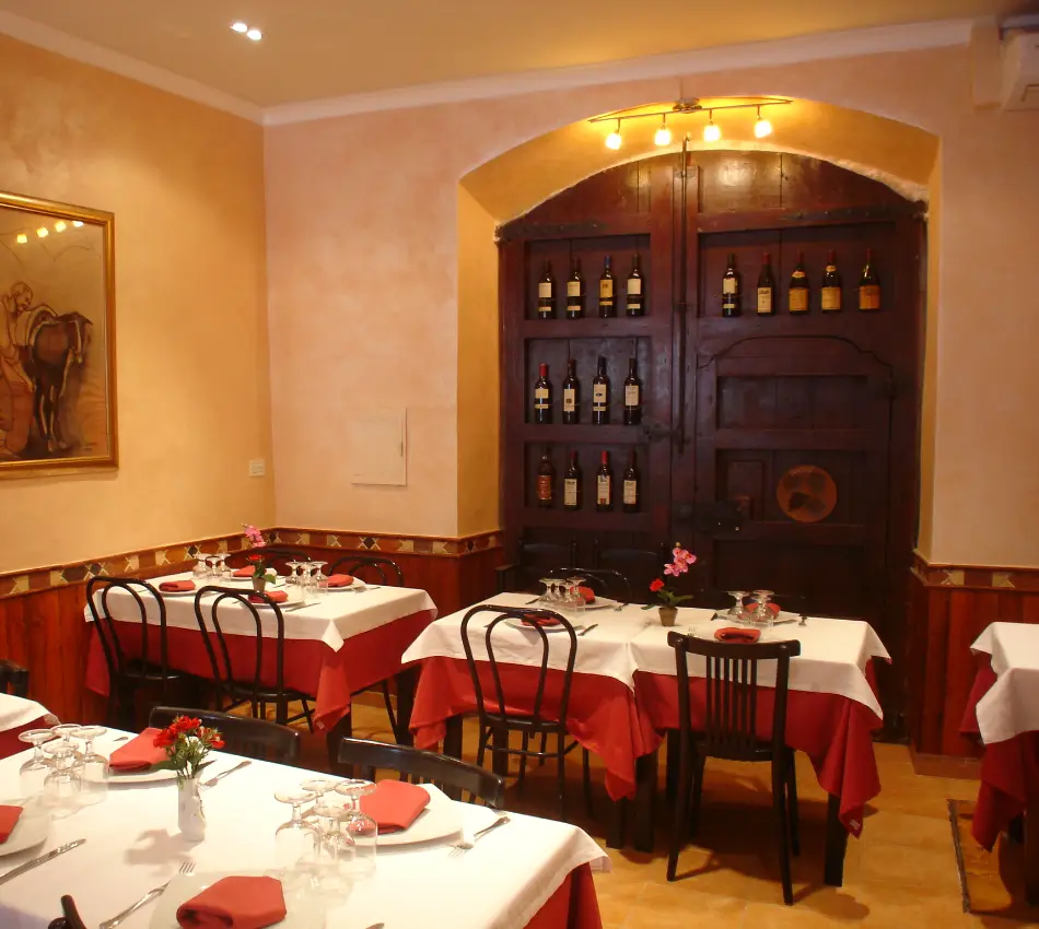 Restaurant acollidor amb taules parades i porta decorada amb ampolles de vi.