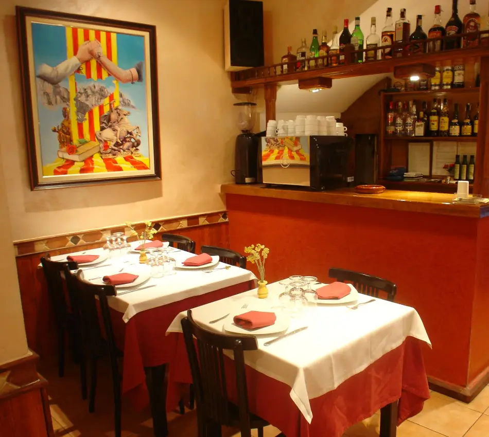 Taula parada en un restaurant amb quadre i prestatgeria al fons.