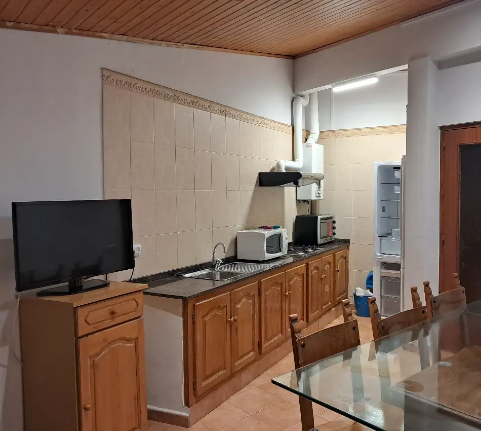 Cuina amb armaris de fusta, taula de vidre, televisi&oacute; i electrodom&egrave;stics b&agrave;sics.