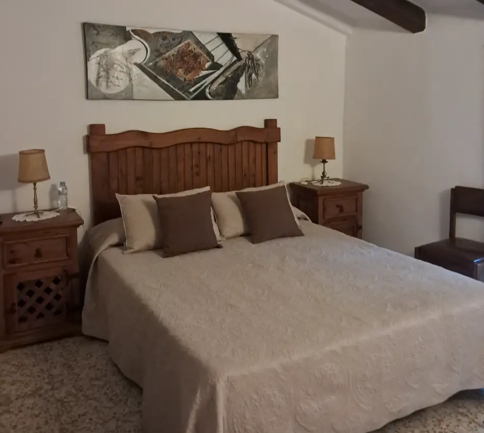 Dormitori amb llit de fusta i tauletes de nit, decorat amb un quadre.