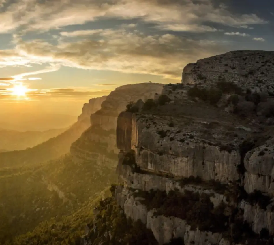 Sortida de sol darrere d'un mass&iacute;s roc&oacute;s amb cel cobert de n&uacute;vols.