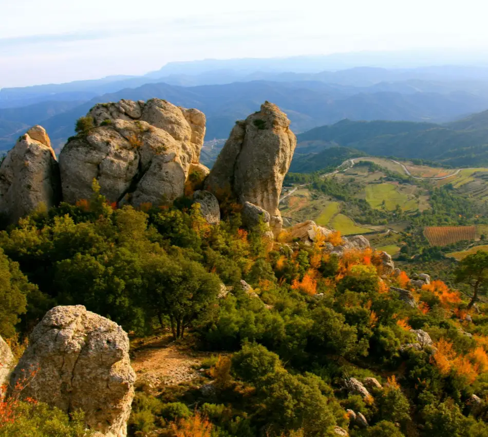 Paisatge muntany&oacute;s amb roques i bosc, vista panor&agrave;mica de camps i muntanyes.