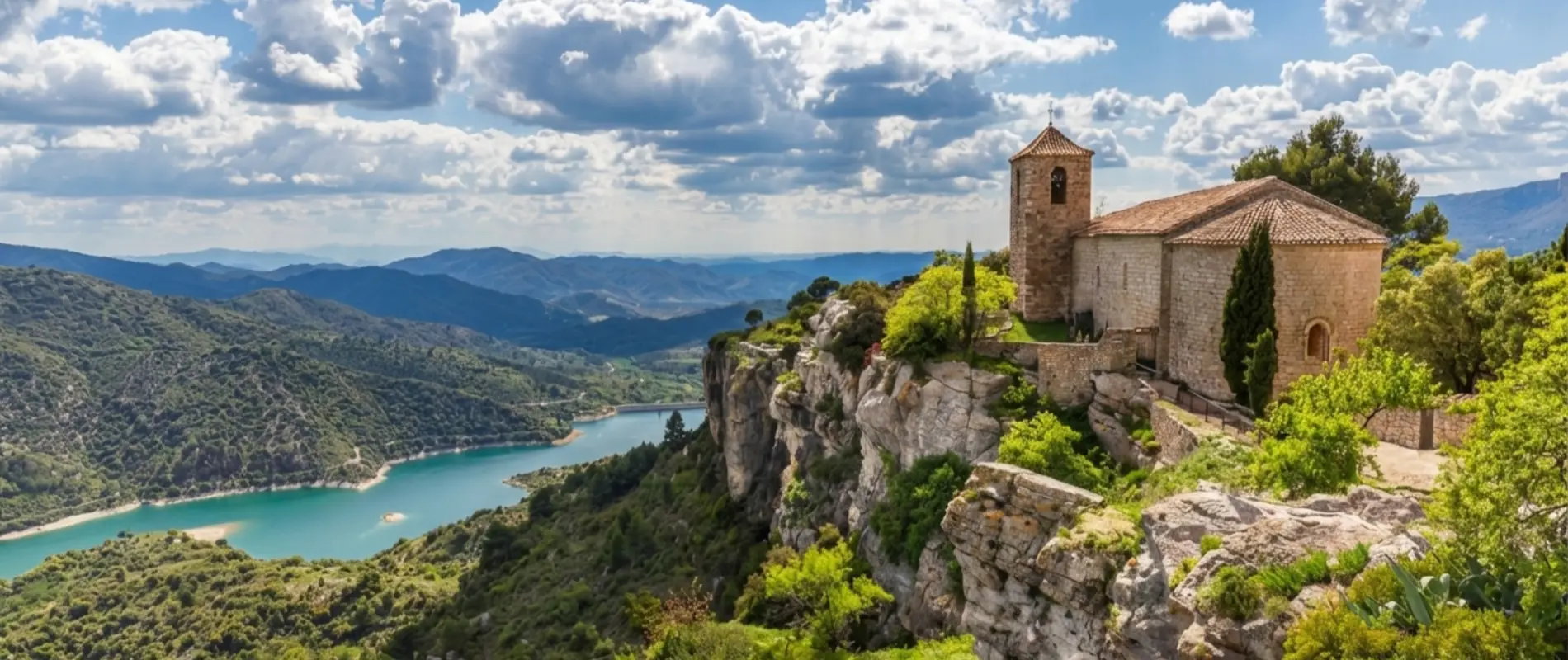 Esgl&eacute;sia sobre un penya-segat amb riu i muntanyes al fons, cel amb n&uacute;vols.