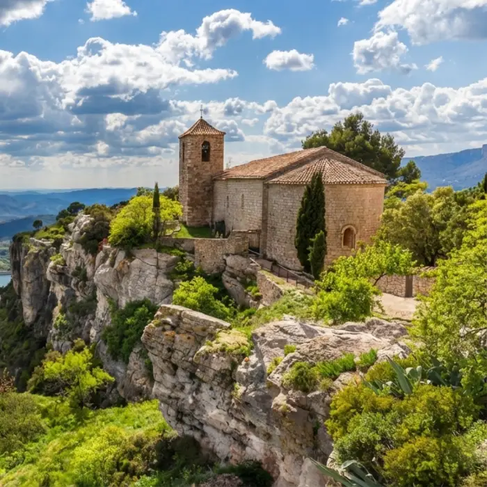 Esgl&eacute;sia medieval sobre un penya-segat amb cel blau i n&uacute;vols.