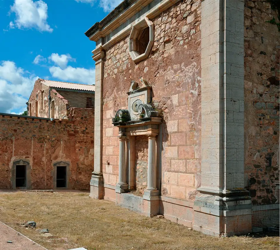 Ru&iuml;nes d'un edifici antic de pedra sota un cel solejat amb alguns n&uacute;vols.