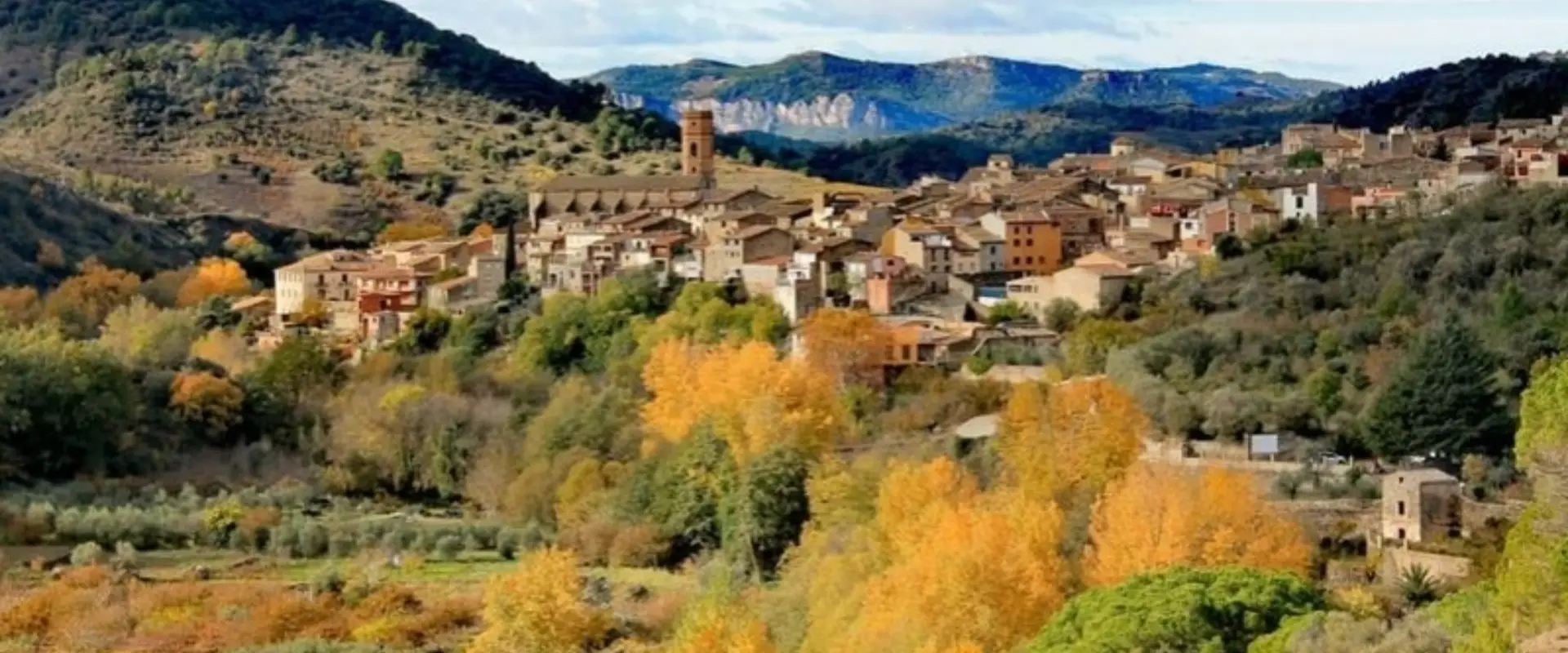 Poble en un paisatge muntany&oacute;s amb arbres de colors tardorals.