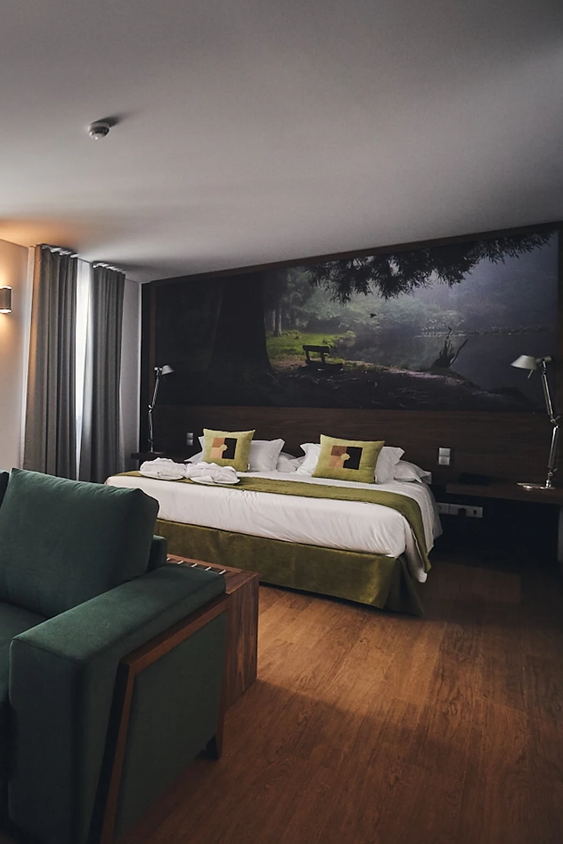 Quarto de hotel moderno com cama, sof&aacute; e mural de floresta na parede.