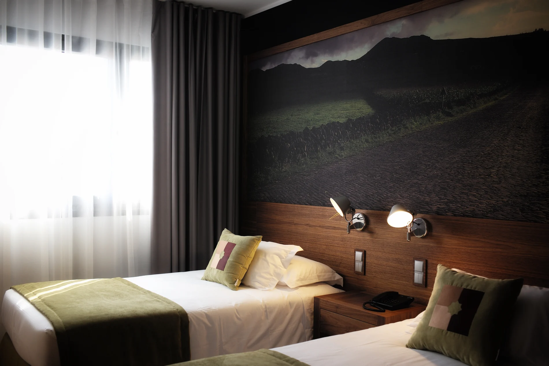 Quarto de hotel com duas camas, travesseiros verdes e luz natural suave.