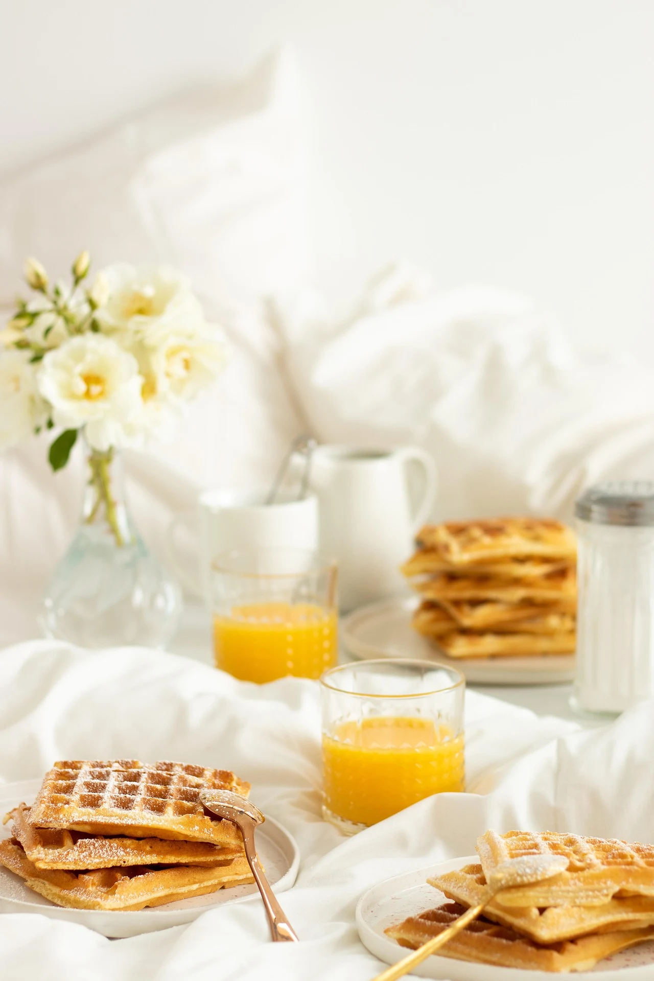 Caf&eacute; da manh&atilde; na cama com waffles e suco de laranja, flores ao fundo.