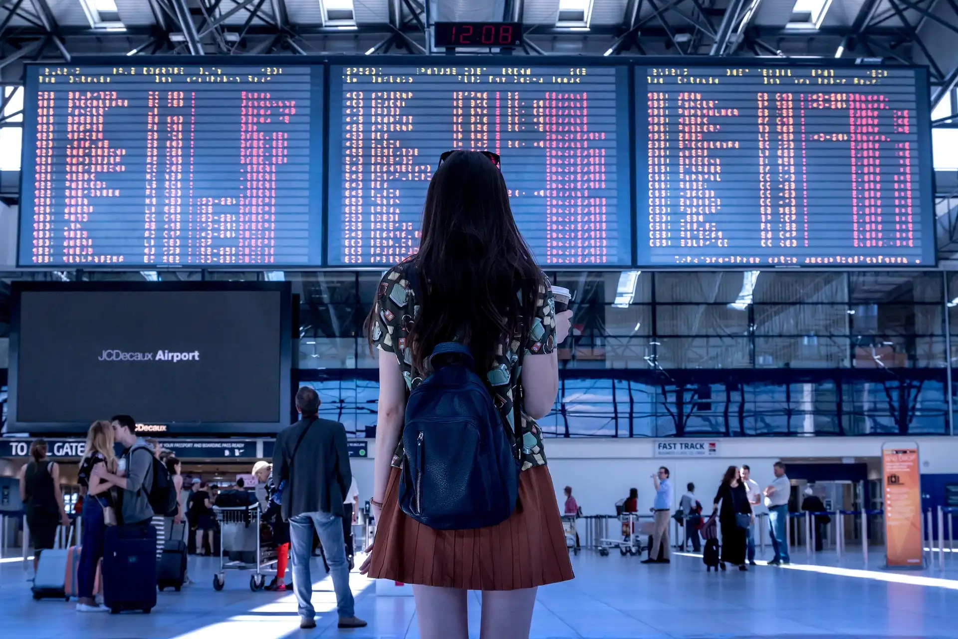 Mulher observando painel de voos em aeroporto movimentado.