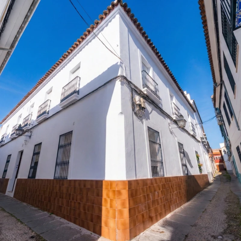 Edificio blanco de esquina con base marr&oacute;n y ventanas con rejas, bajo un cielo despejado.